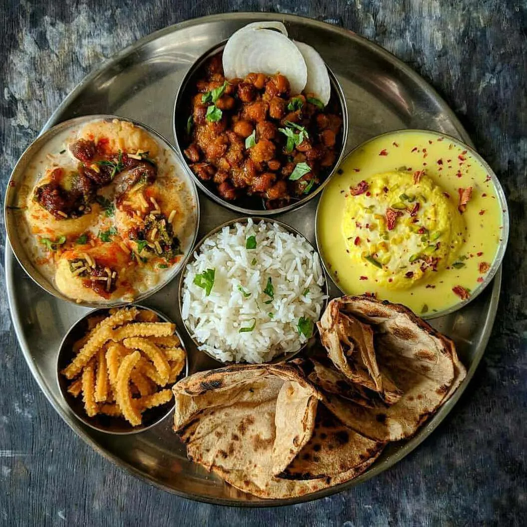 Steel tray with chole, kadhi, rice, roti, and an Indian sweet