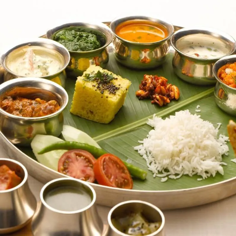 Gujarati vegetarian thali with rice, dal, sabzi, and dhokla in steel bowls