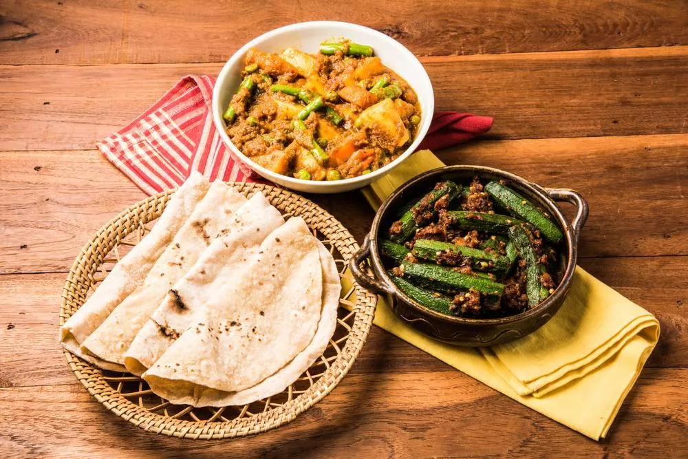 Rotis in a basket beside bowls of mixed vegetables and bhindi