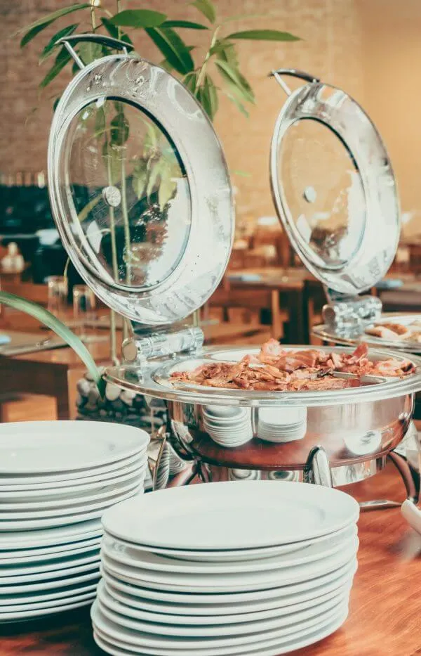 Open chafing dishes and stacked plates on a cafeteria counter