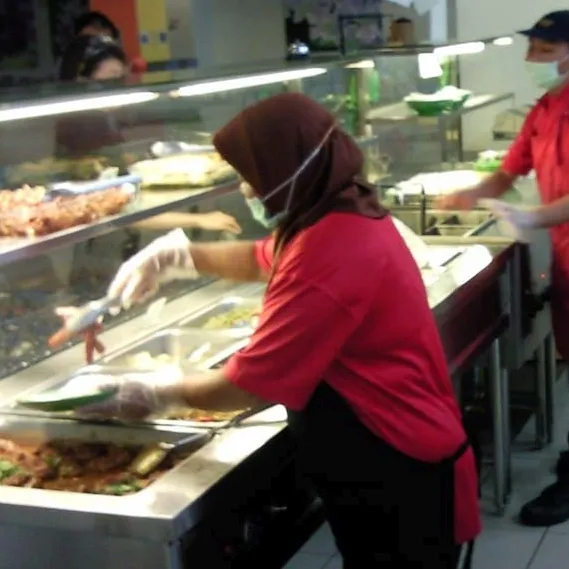 Staff serving food from steel trays on a canteen line
